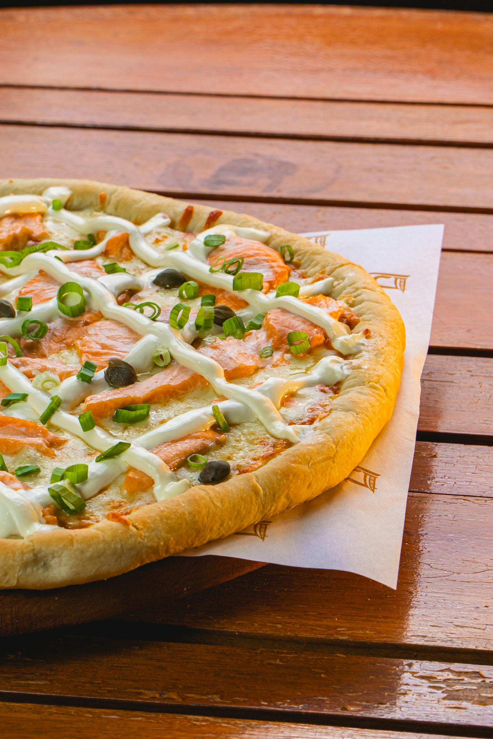 A delicious gourmet salmon pizza with cream cheese and capers on a wooden table.